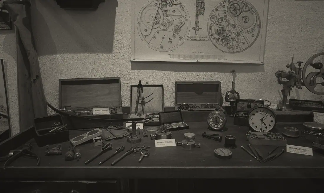 A watchmaker's bench beneath a wall chart of movement diagrams.