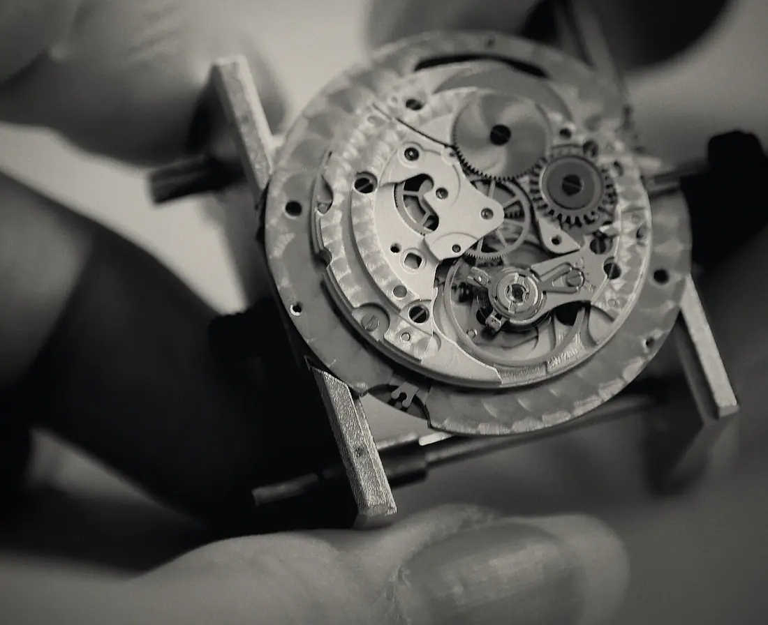 Gloved fingertips holding a bare mechanical movement.