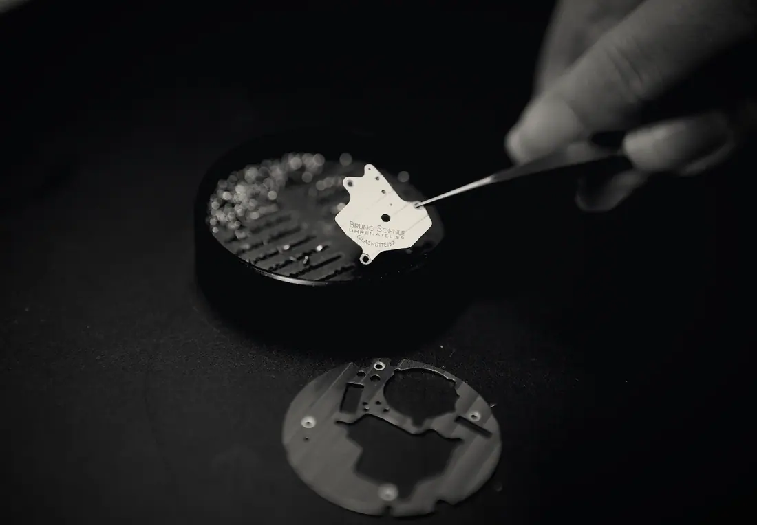 A watchmaker places a component with tweezers onto a movement holder.